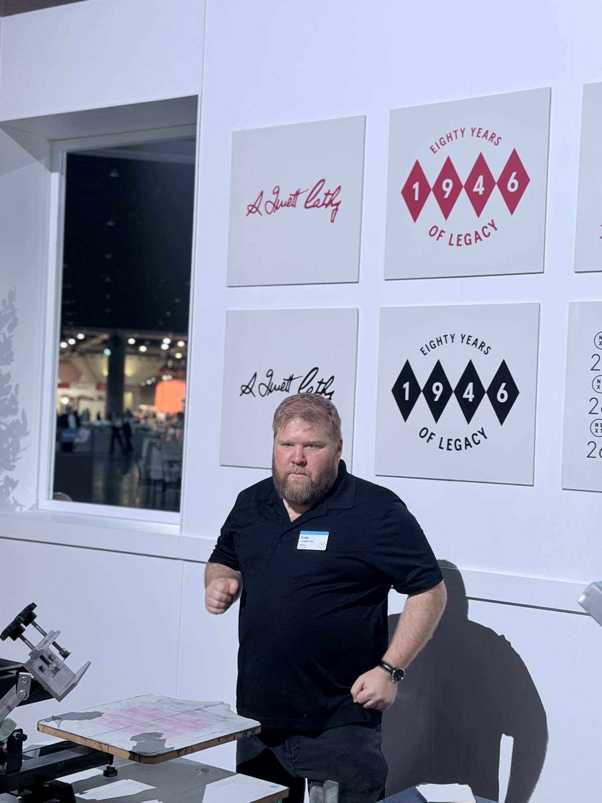 Print operator working a manual press inside a white trade show booth